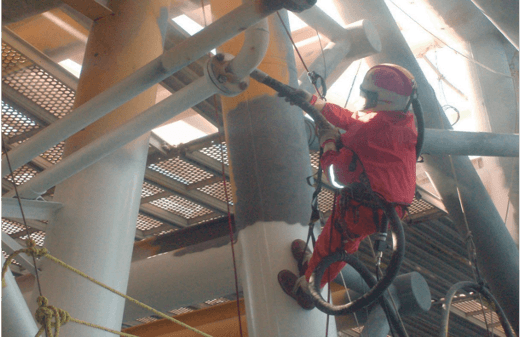 Técnico suspendido en cuerdas limpia una columna metálica dentro de una estructura industrial
